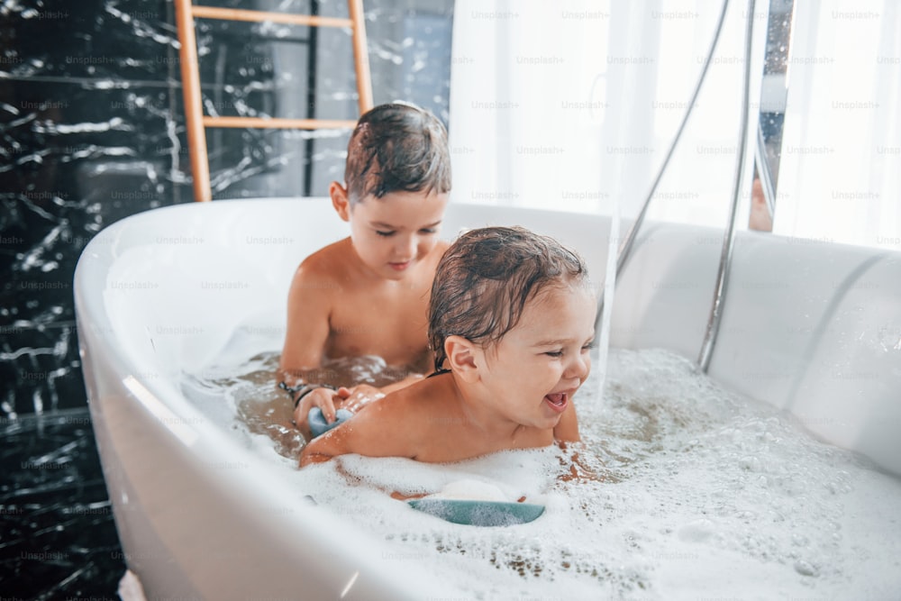 Dos niños divirtiéndose y lavándose en la bañera de su casa. Ayudándonos unos a otros.