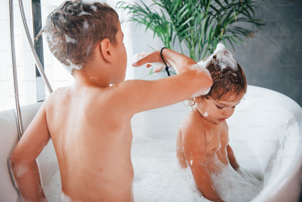 Duas crianças se divertindo e se lavando no banho em casa.