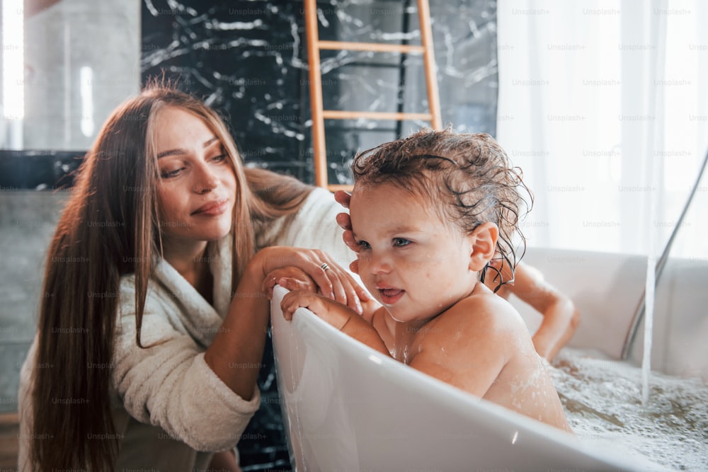 Young mother helps her son and daughter. Two kids washing in the bath.