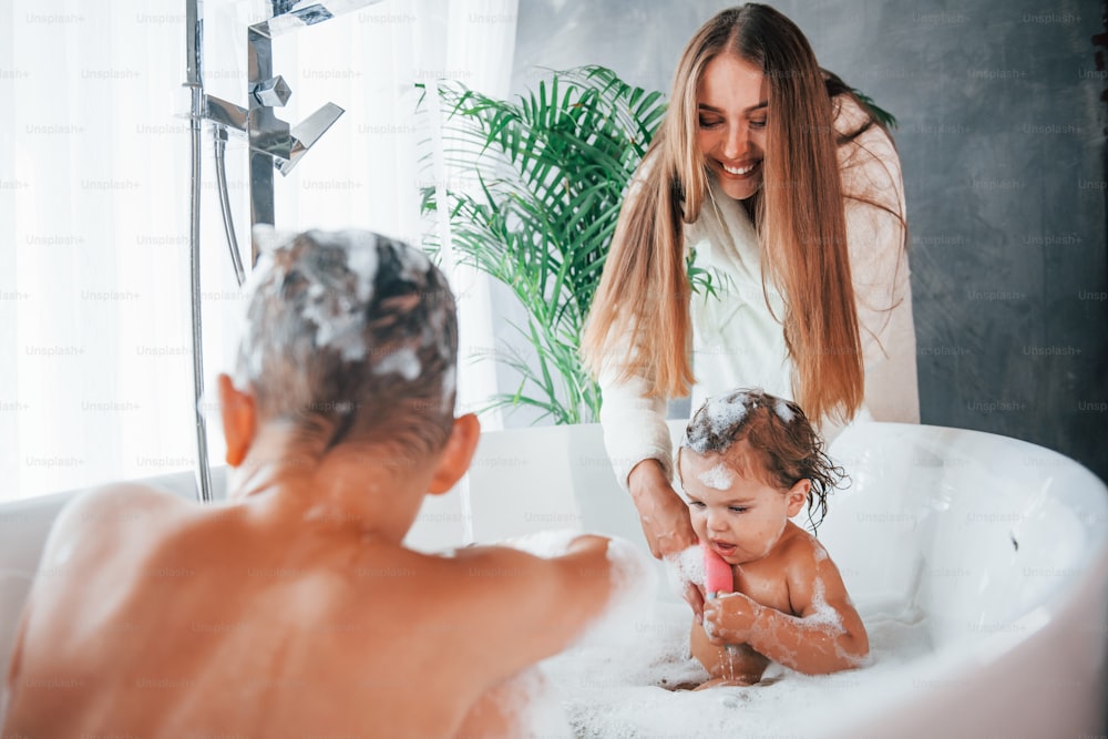Spaß. Die junge Mutter hilft ihrem Sohn und ihrer Tochter. Zwei Kinder waschen sich in der Badewanne.