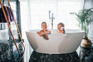 自宅でお風呂で体を洗って楽しんでいる2人の子供。カメラに向かってポーズをとる。