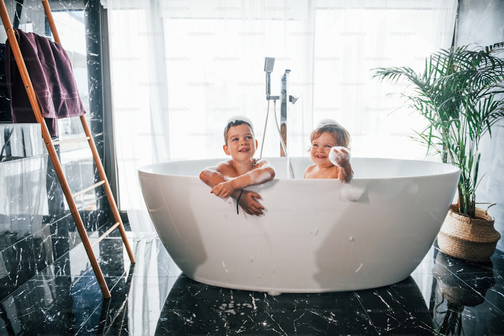 Zwei Kinder haben Spaß und waschen sich zu Hause in der Badewanne. Für eine Kamera posieren.