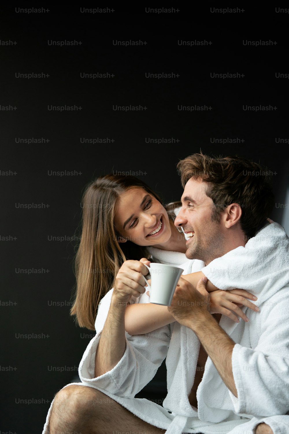 Happy young couple in white bathrobes drinking coffee together. Hotel, travel, relationships, and happiness concept