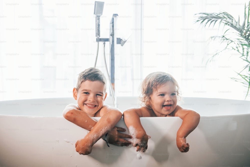 自宅でお風呂で体を洗って楽しんでいる2人の子供。カメラに向かってポーズをとる。