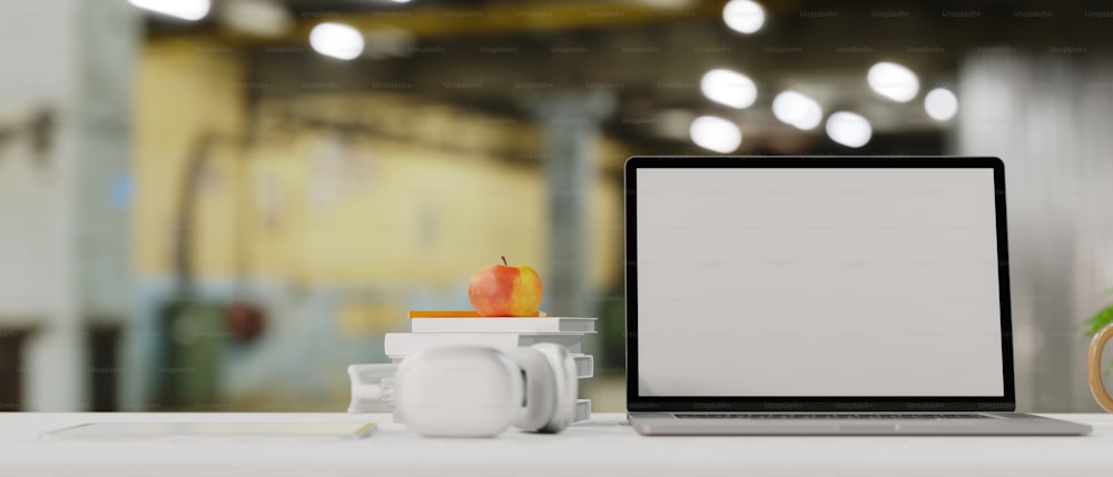 ラップトップの空の画面のモックアップ、ヘッドフォン、本、トップテーブルの上のリンゴ、背景にぼやけたオフィス、3Dレンダリング、3Dイラストを使用したブランドの白いコピースペース