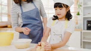 Happy smiling young Asian Japanese family with preschool kids have fun cooking baking pastry or pie for breakfast meal in modern kitchen home in the morning. Doing bakery knead dough and bake cookies.