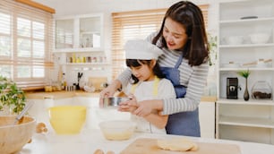La feliz familia japonesa asiática joven sonriente con niños en edad preescolar se divierte cocinando, horneando, pastelería o pastel para la comida del desayuno en la cocina moderna en casa por la mañana. Haciendo panadería, amasar masa y hornear galletas.