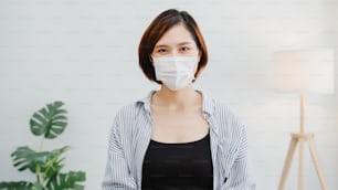 Une femme d’affaires asiatique porte un masque facial, une distanciation sociale en situation de prévention du virus, regardant la caméra souriant sous un masque chirurgical, de retour au travail dans un espace de travail au bureau. Mode de vie après le coronavirus.