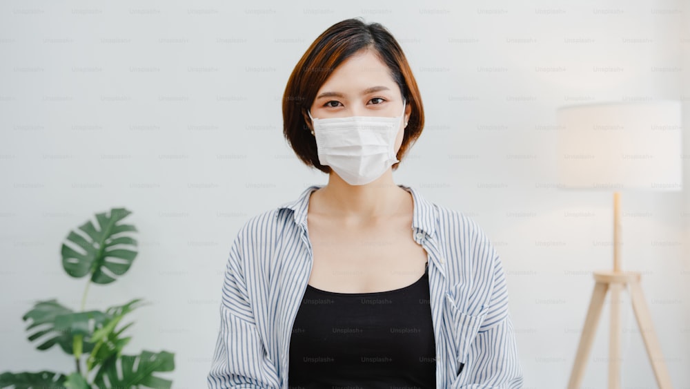 Empresária asiática usa máscara facial distanciamento social em situação de prevenção ao vírus olhando para câmera sorrindo sob máscara cirúrgica de volta ao trabalho no espaço de trabalho do escritório. Estilo de vida após o corona vírus.