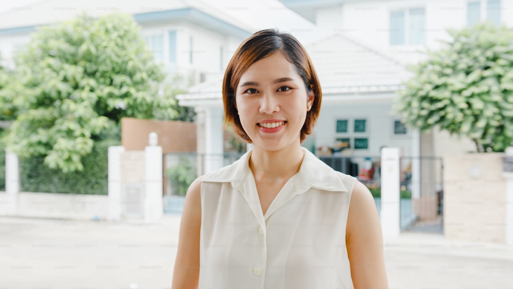 Glückliche junge asiatische Frau, die glücklich lächelt und in die Kamera schaut, während sie sich auf der Straße in der modernen Stadt entspannt. Lifestyle-Frau bei Außenhauskonzept.
