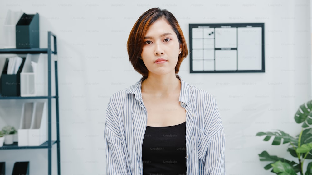 Portrait of beautiful executive businesswoman smart casual wear looking at camera and smiling, happy in modern office workplace. Young Asia lady talk to colleague in video call meeting at home.