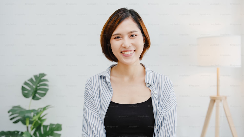 Portrait of beautiful executive businesswoman smart casual wear looking at camera and smiling, happy in modern office workplace. Young Asia lady talk to colleague in video call meeting at home.