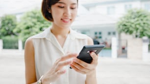 Jolie jeune femme d’affaires asiatique utilisant un téléphone portable vérifiant les médias sociaux Internet, discutant avec des amis à l’extérieur dans la rue de la ville. Mode de vie nouvelle normalité après le coronavirus et la distanciation sociale.