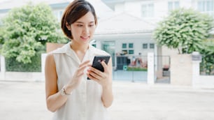 Attraente giovane donna d'affari asiatica che utilizza il telefono cellulare controllando i social media internet, chattando con gli amici fuori per strada in città. Stile di vita nuovo normale dopo il coronavirus e il distanziamento sociale.