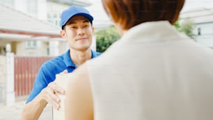 Young Asia postal delivery courier man in blue shirt handling parcel boxes for sending to customer at house and Asian female receive delivered package outdoors. Package shopping food delivery concept.