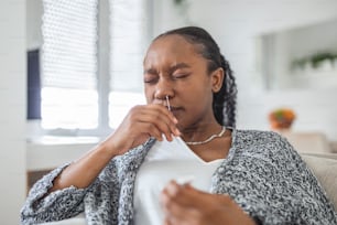 Mujer afroamericana usando un hisopo de algodón mientras se hace la prueba PCR de coronavirus en casa. Mujer usando prueba de diagnóstico rápido de coronavirus. Mujer joven en casa usando un hisopo nasal para COVID-19.