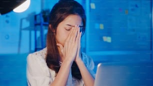 Freelance Asia women using laptop hard work at new normal home office. Working from house overload at night, remotely work, self isolation, social distancing, quarantine for corona virus prevention.