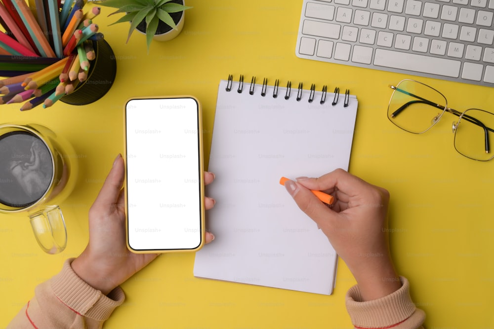 Female designer using mobile phone and writing on empty notebook.