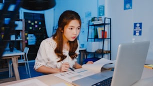 Mujeres asiáticas independientes que usan una computadora portátil para trabajar duro en la nueva oficina en casa normal. Sobrecarga de trabajo desde casa por la noche, trabajo remoto, autoaislamiento, distanciamiento social, cuarentena para la prevención del coronavirus.