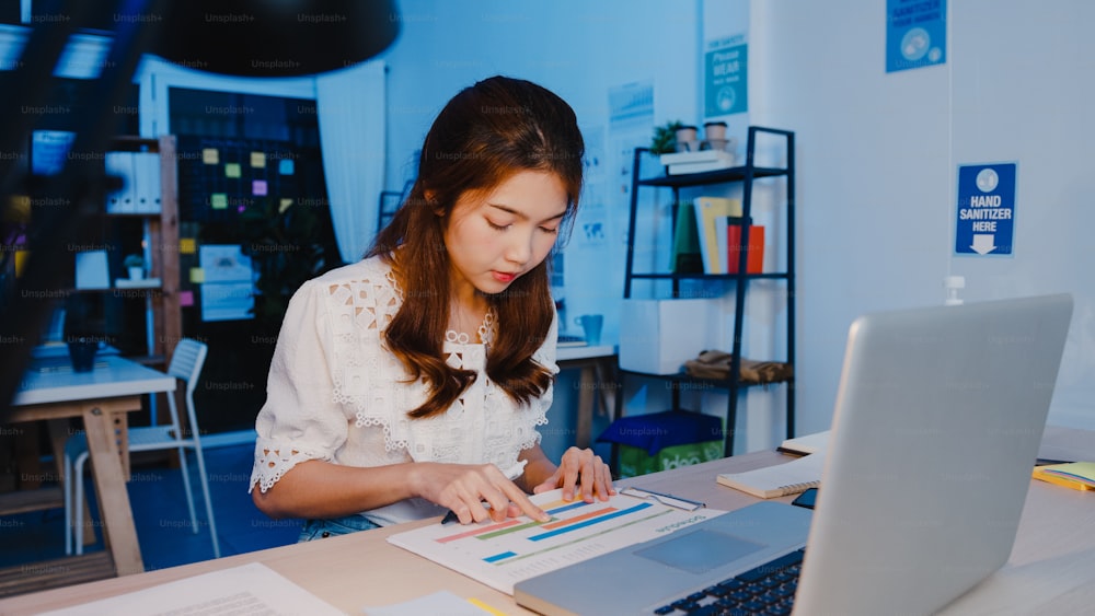 Freelance Asia women using laptop hard work at new normal home office. Working from house overload at night, remotely work, self isolation, social distancing, quarantine for corona virus prevention.