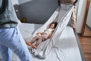 Ready for the entertainment. Close up view of the cute multiracial girl laying wrapped at the blanket and waiting while her parents started swinging her. Stock photo