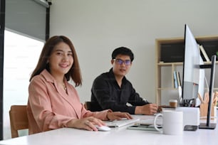 Two young business people sitting together in modern office and smiling to camera.