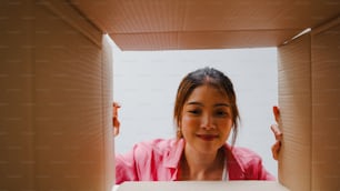 Excited Asian young woman unpack opening huge carton box and looking inside new gift at home. Happy millennial female client satisfied with ordered purchase. Delivery and online shopping concept.