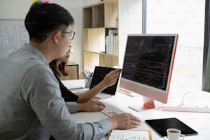 Equipo de negocios discutiendo y analizando gráficos de negociación bursátil con computadora.