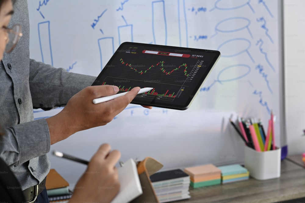 Zwei Investoren, die gemeinsam Börseninvestitionen über ein digitales Tablet im Büro analysieren.