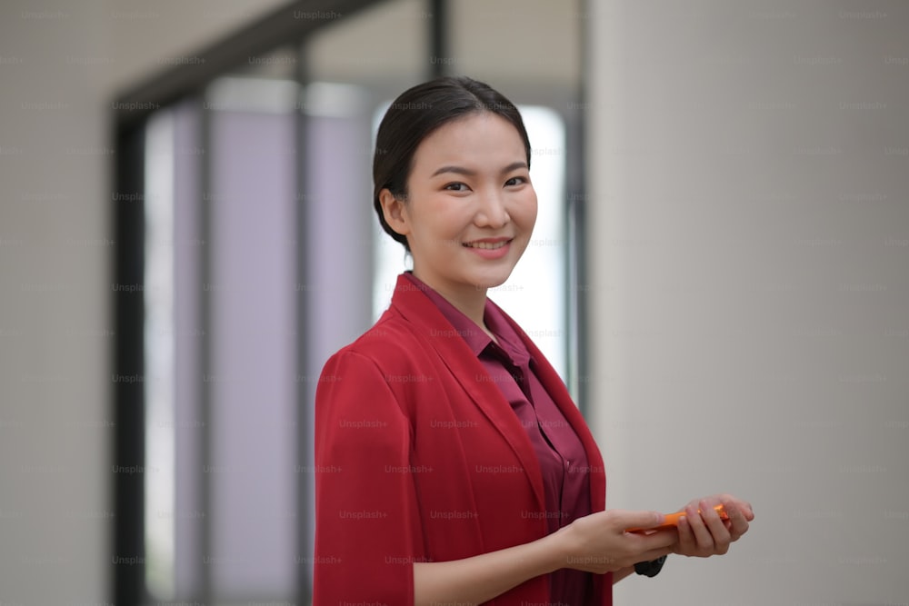 Confident businesswoman holding mobile phone and smiling to camera.