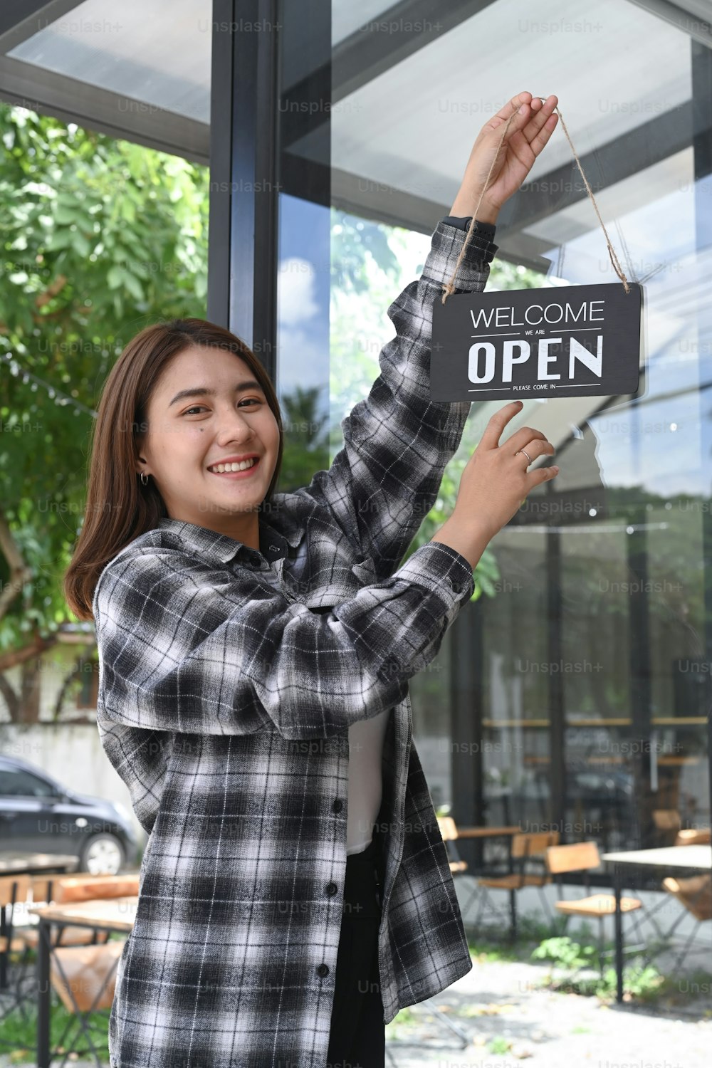 Smiling Asian woman turning open sign broad on the door glass and ready to service.