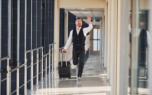 Un hombre vestido de gala y con equipaje corre hacia adelante y está ocupado para un avión.