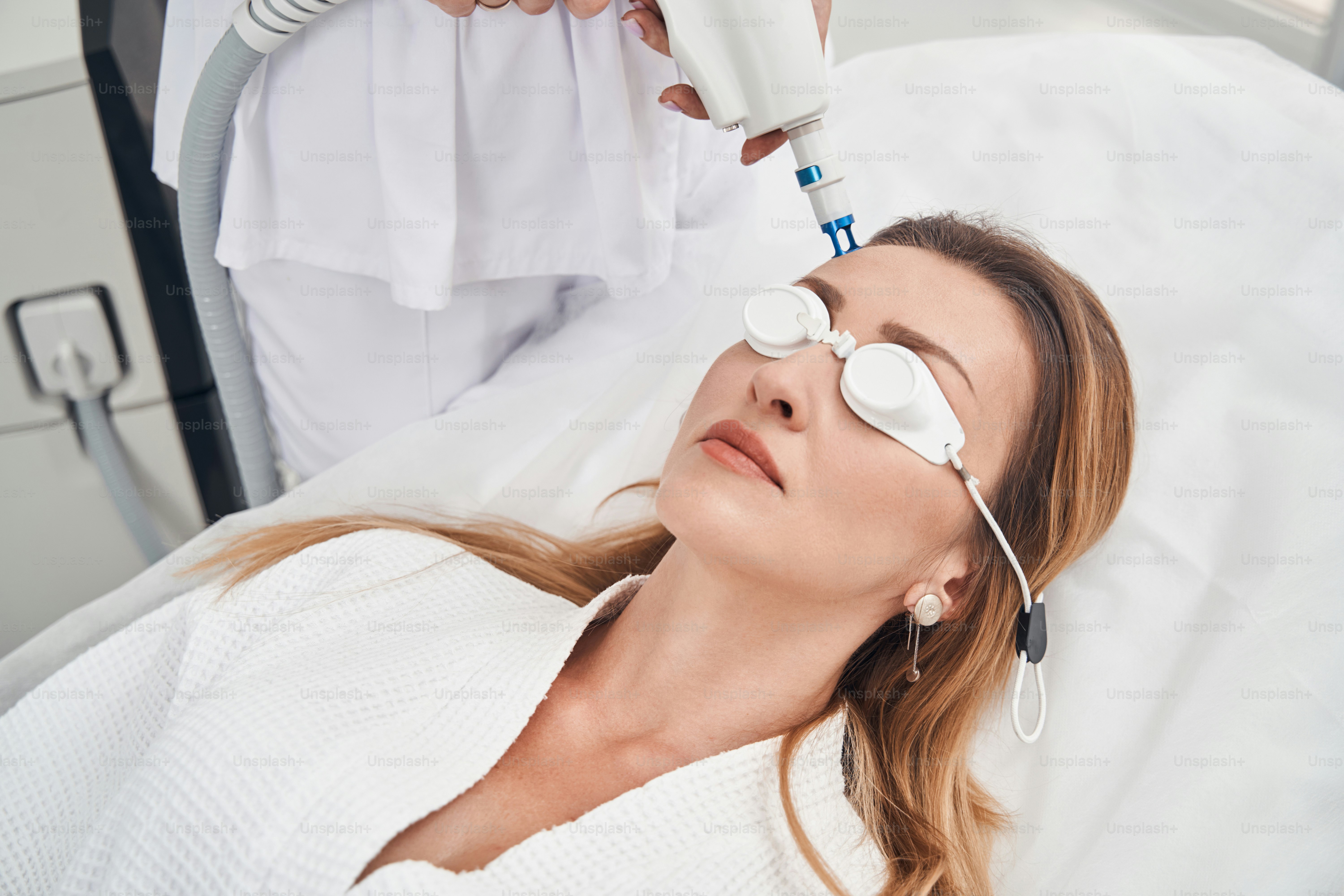 Vista dall'alto della femmina sdraiata sul divano mentre il cosmetologo sta facendo la regolazione laser per lei in clinica