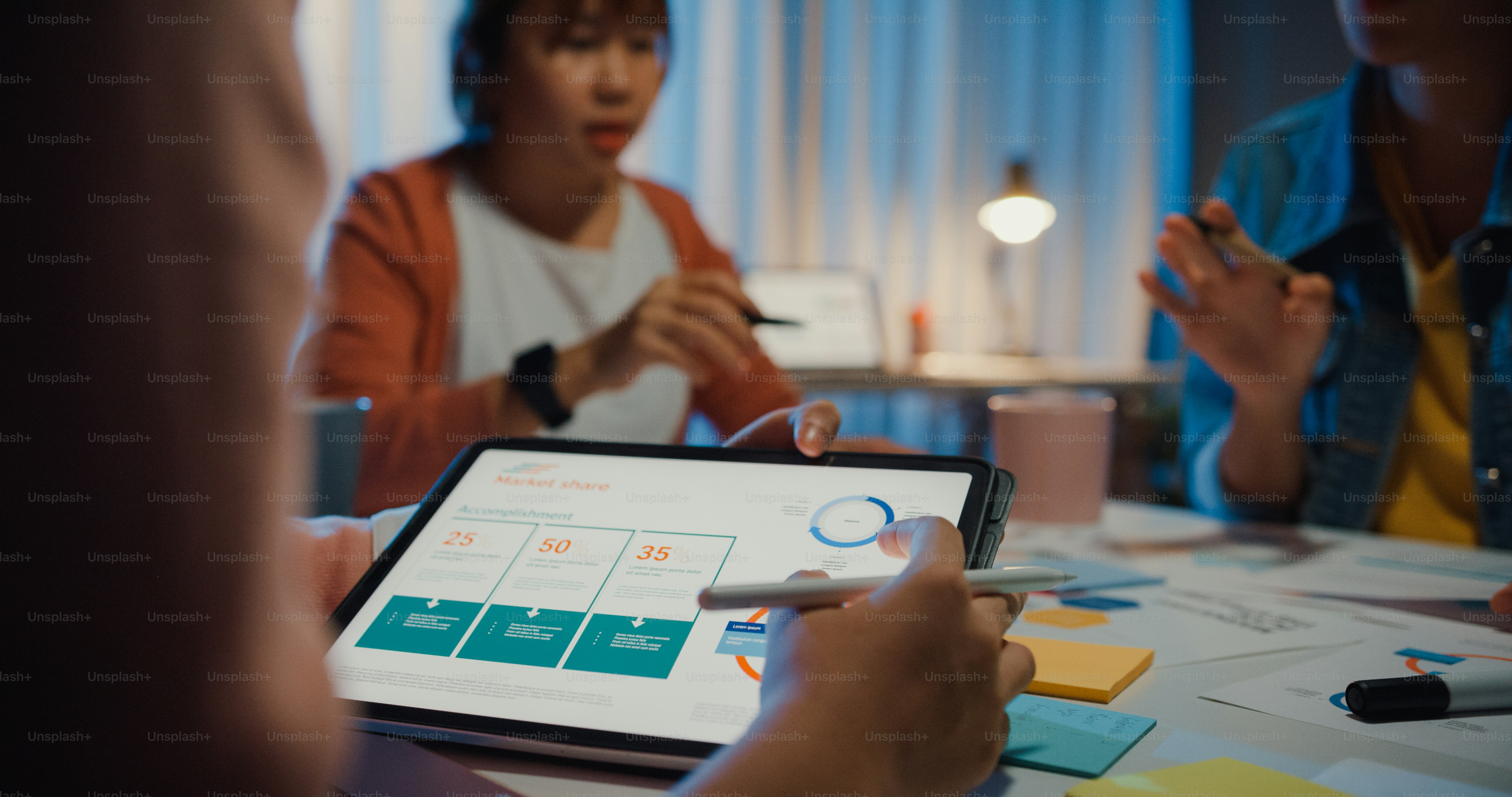 A person pointing at a tablet displaying business charts during a team meeting