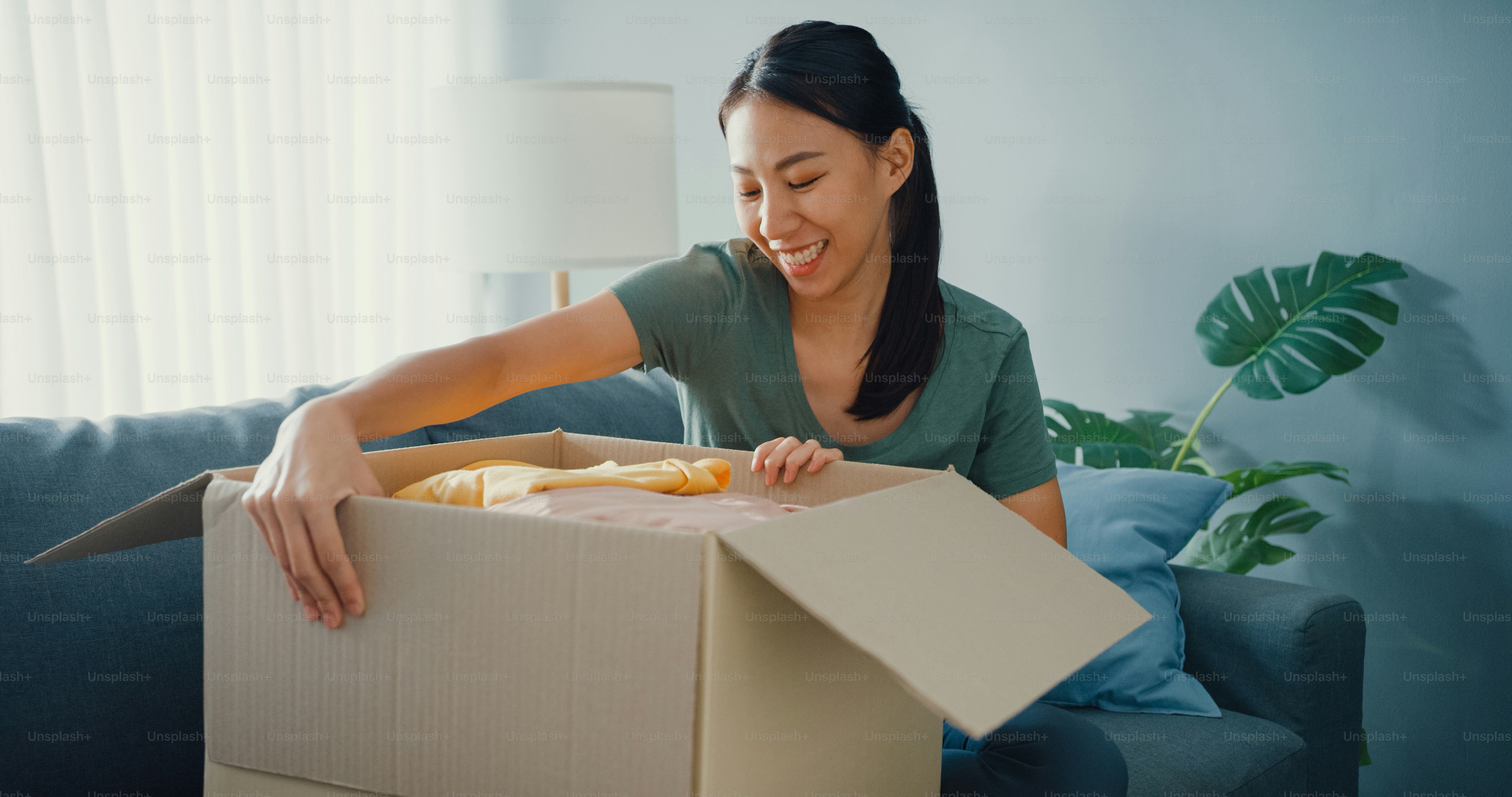 Feliz paquete de caja de cartón abierto de la señora asiática emocionante y disfruta probando y combinando con la calidad del producto de tela de moda del mercado en línea en la sala de estar de casa. Concepto de compra y entrega en línea.