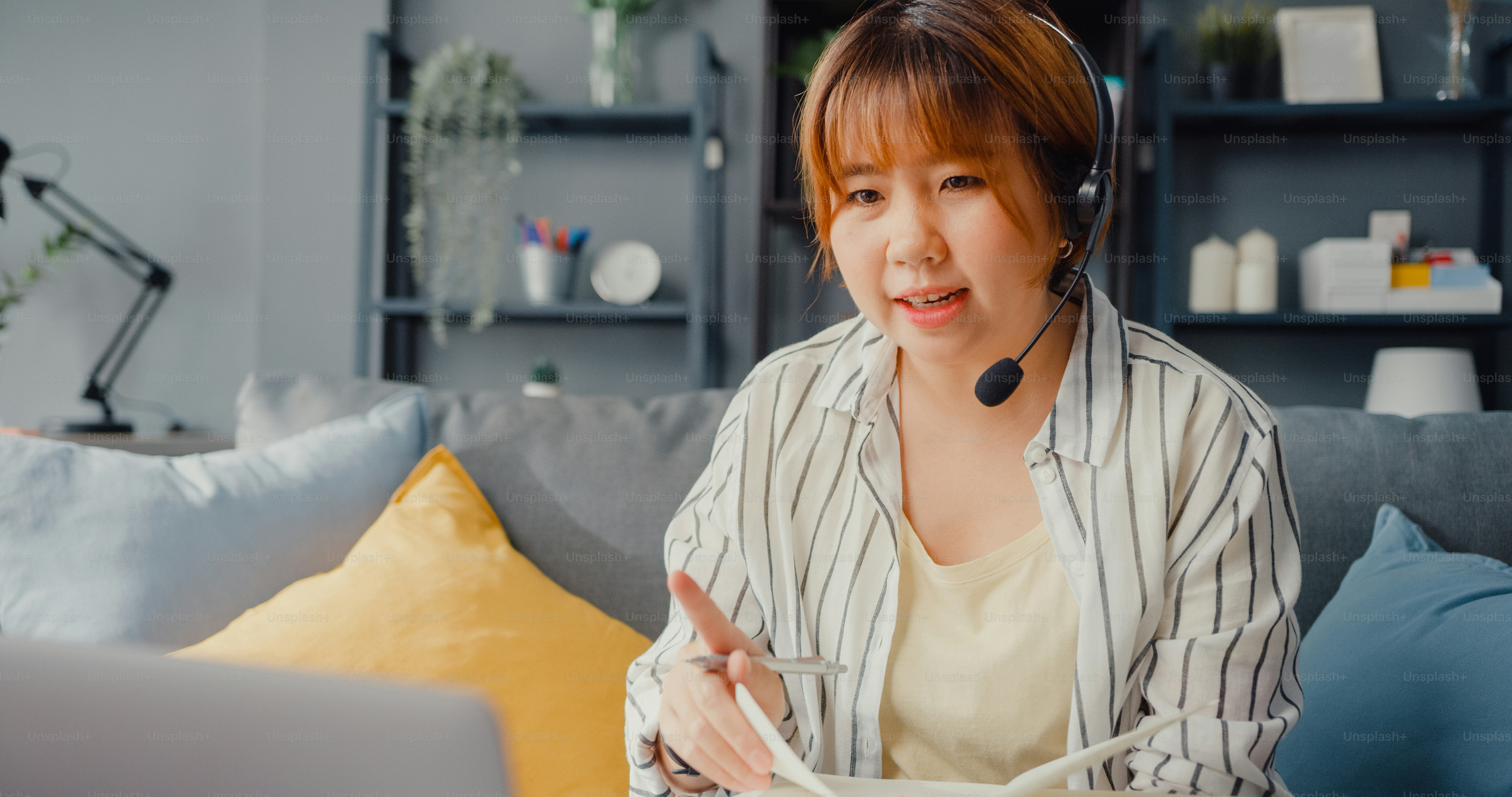 Asia businesswoman using laptop talk to colleagues about plan in video call while working from house at living room. Remotely at workplace, social distancing, quarantine for corona virus prevention.