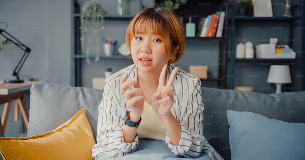 Asia businesswoman using laptop talk to colleagues about plan in video call while working from house at living room. Remotely at workplace, social distancing, quarantine for corona virus prevention.