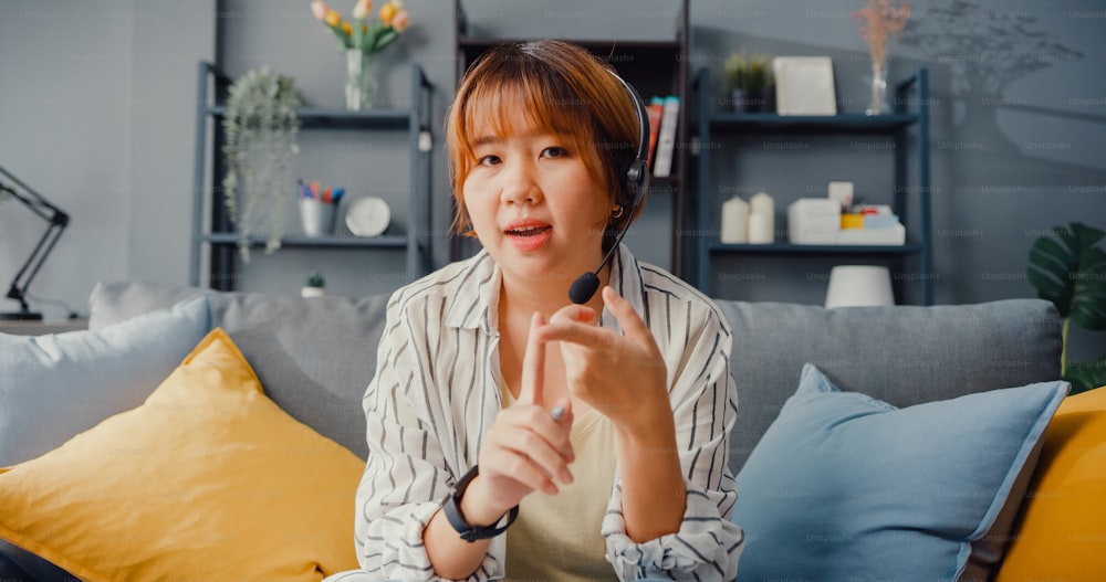L'imprenditrice asiatica che usa il laptop parla con i colleghi del piano in videochiamata mentre lavora da casa in soggiorno. Da remoto sul posto di lavoro, distanziamento sociale, quarantena per la prevenzione del coronavirus.