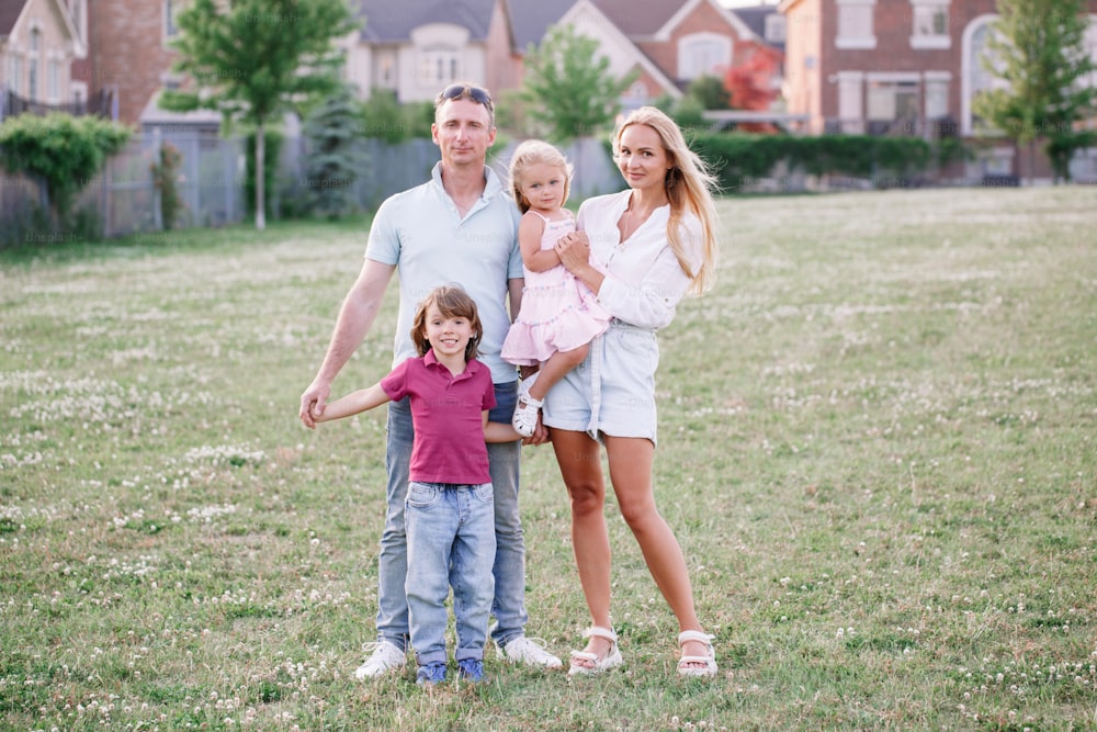 Happy Caucasian family with two kids boy and girl walking in park outdoor on summer day. Beautiful young family with daughter and son standing on meadow outside. Parents with children kids.