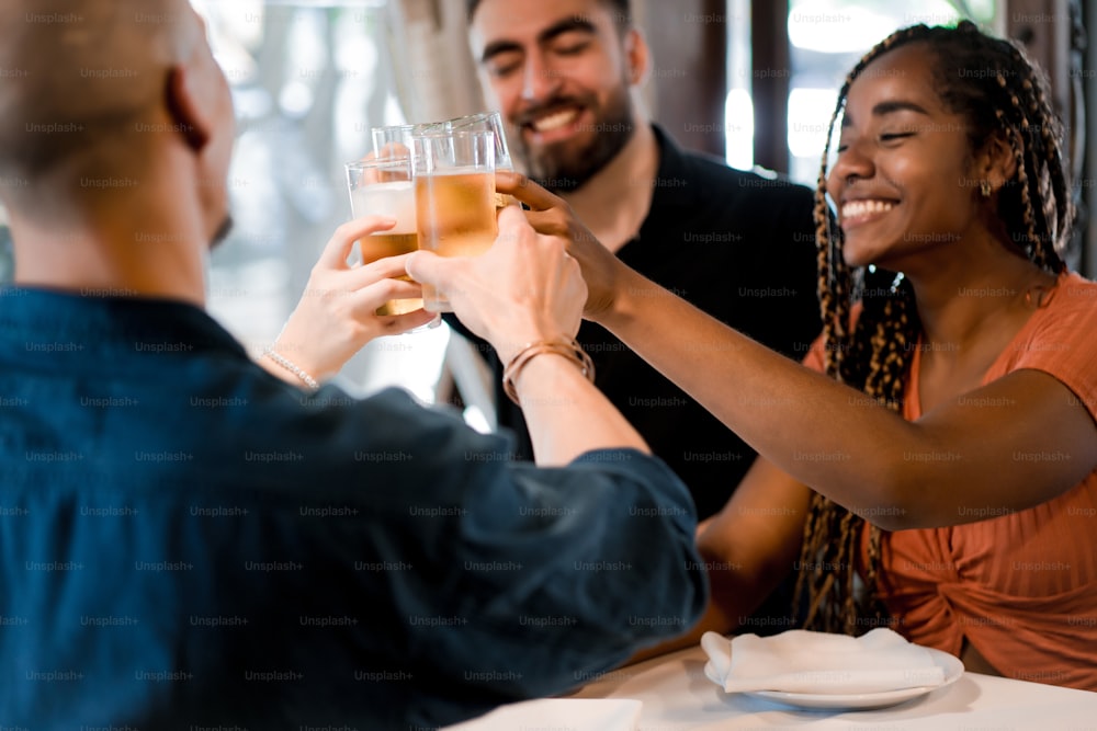 Grupo de amigos diversos brindando con vasos de cerveza mientras disfrutan de una comida juntos en un restaurante. Concepto de amigos.