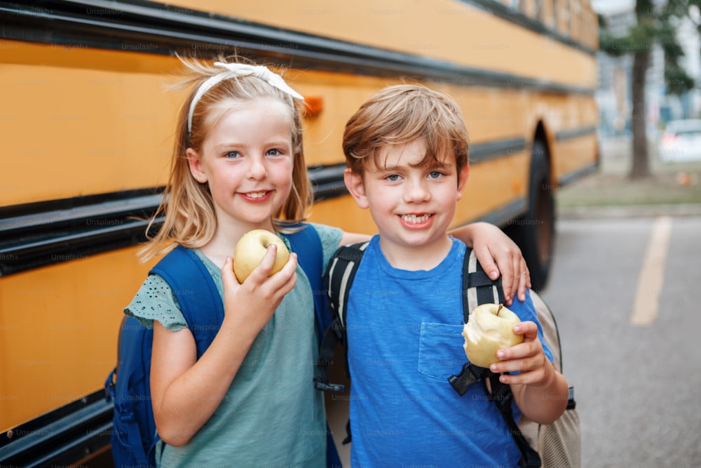 Bambini, ragazzi e ragazze, studenti, amici che mangiano mele spuntino sano dallo scuolabus giallo all'aperto. Istruzione e ritorno a scuola a settembre. Compagni di classe che si incontrano dopo la pausa estiva.