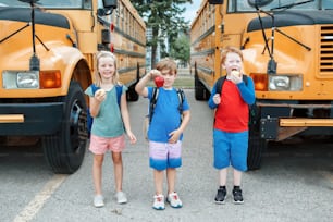 Kinder Jungen und Mädchen Freunde essen Äpfel gesunden Snack mit gelben Schulbus im Freien. Bildung und Rückkehr in die Schule im September. Klassenkameraden treffen sich nach den Sommerferien.