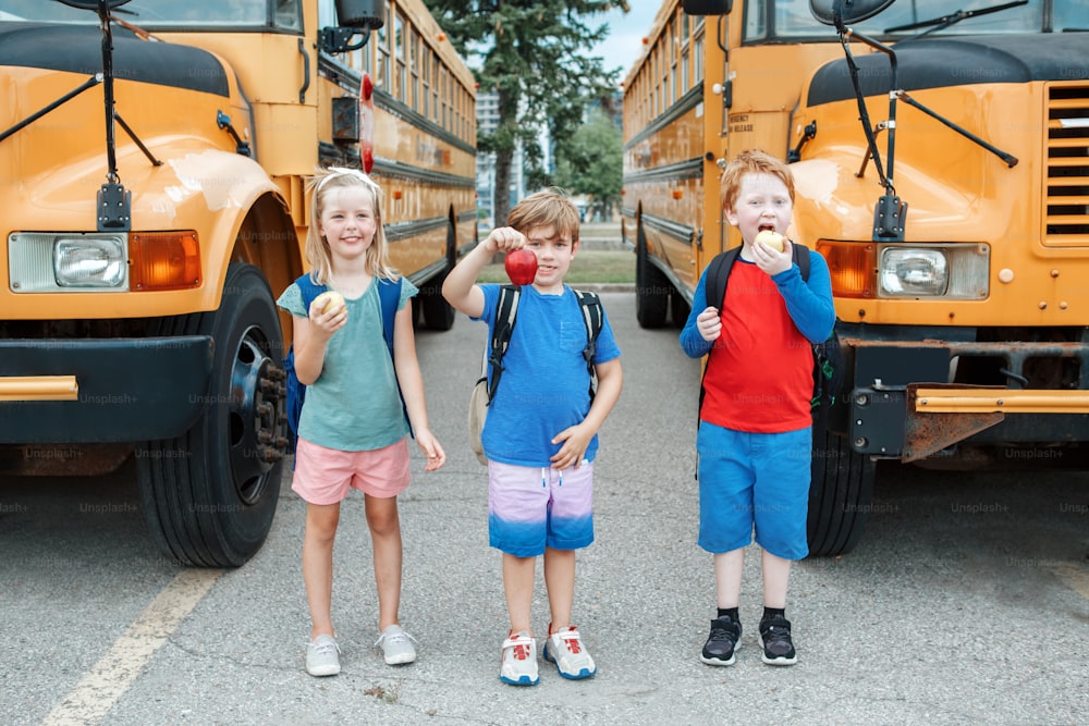 Bambini, ragazzi e ragazze, studenti, amici, che mangiano mele, spuntino sano dallo scuolabus giallo all'aperto. Istruzione e ritorno a scuola a settembre. Compagni di classe che si incontrano dopo la pausa estiva.