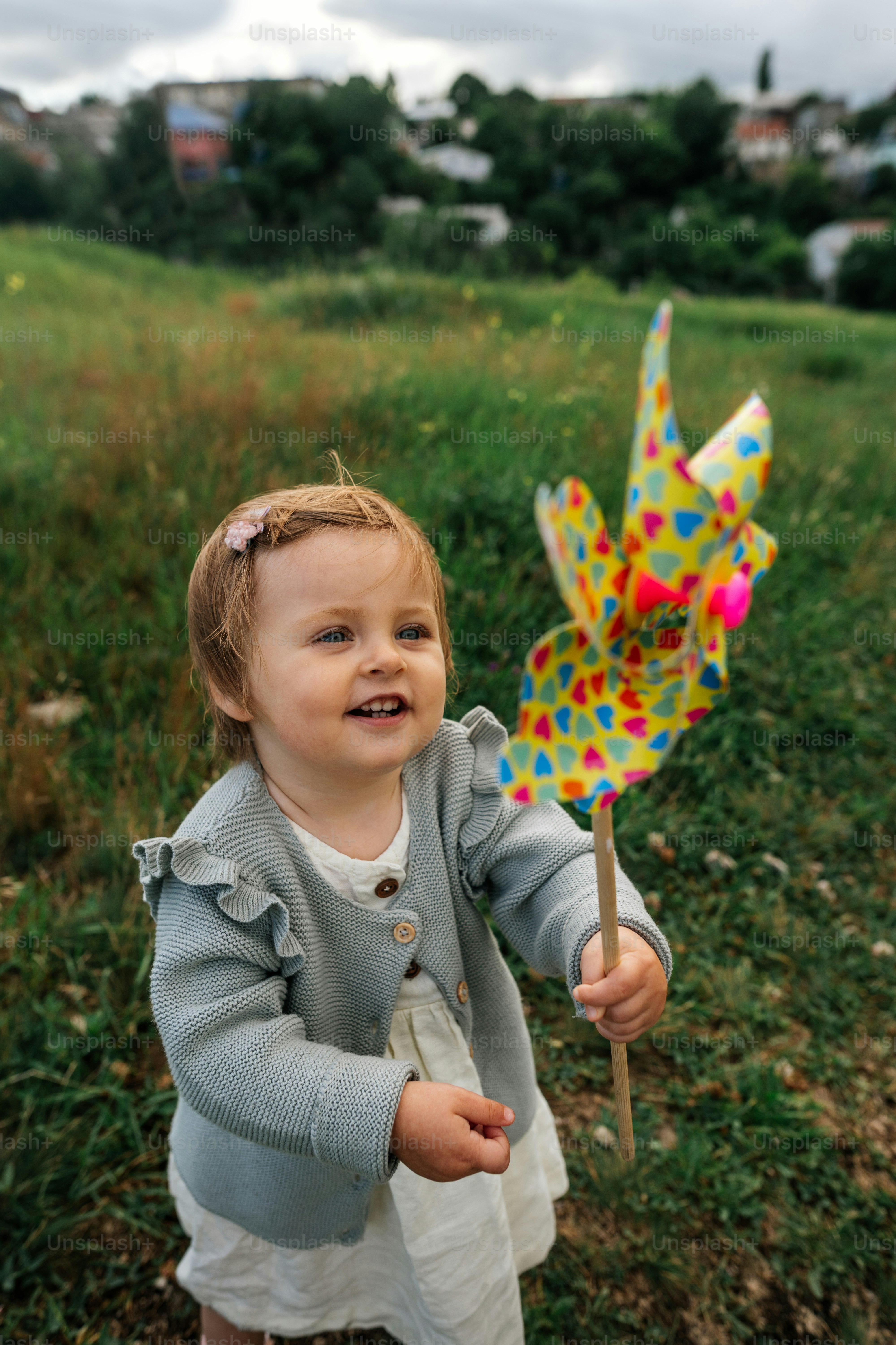 Retrato de una adorable niña pequeña con ropa informal jugando con un molino de viento de juguete al aire libre