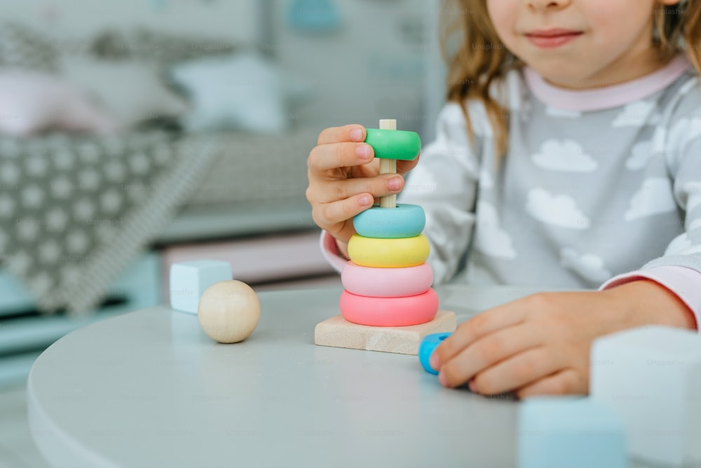 Primo piano della bambina che indossa il pigiama che gioca con la piramide del giocattolo di legno seduta al tavolo nella stanza dei bambini. Concetto di giocattoli ecologici naturali. Messa a fuoco selettiva.