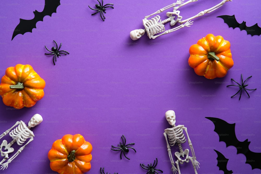 Frame of Halloween decorations on purple background. Flat lay skeletons, bats silhouettes, spiders, pumpkins. Happy Halloween concept.