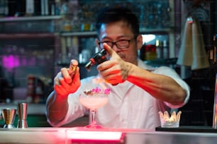 Confidence Asian woman sitting at bar counter drinking alcoholic drink and talking to barman in nightclub. Male mixologist bartender preparing alcohol drink to customer. Small business bar and city nightlife concept