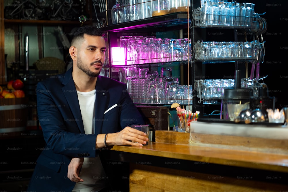 Portrait of Handsome Caucasian man sitting at bar counter holding whiskey glass with ice and enjoy drinking tasty alcoholic drink from barman in nightclub. Nightlife holiday party celebration and small business concept