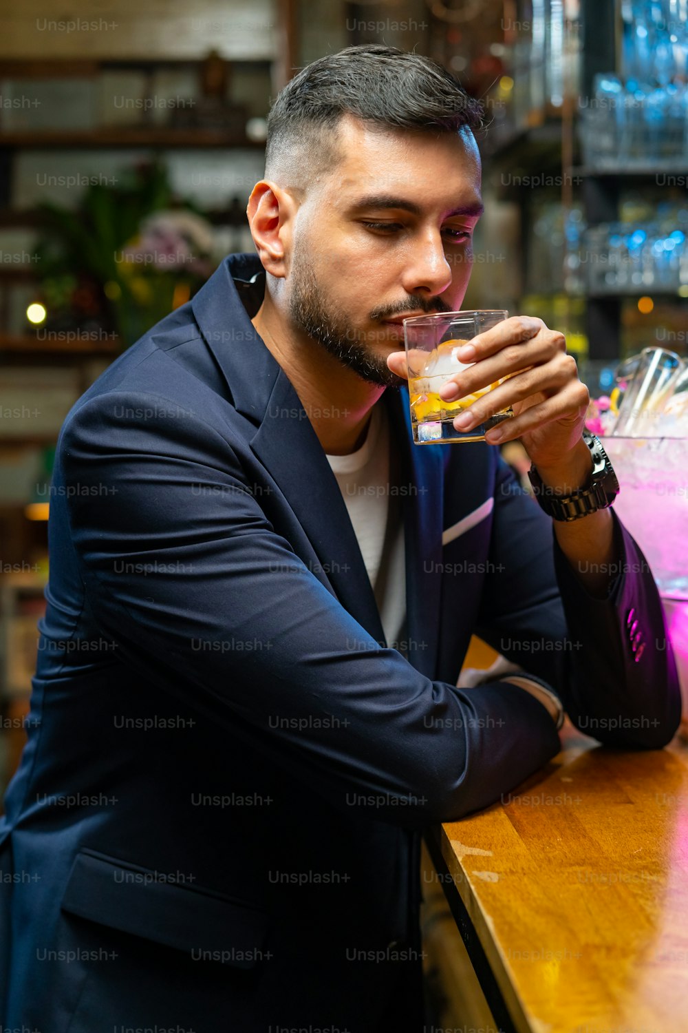 Portrait d’un bel homme caucasien assis au comptoir du bar tenant un verre de whisky avec de la glace et appréciant de boire une boisson alcoolisée savoureuse du barman dans la boîte de nuit. Célébration de fête de vacances de la vie nocturne et concept de petite entreprise