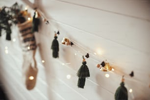Elegante ghirlanda natalizia con campane, calza rustica con ramo di abete e luci natalizie su parete in legno. Camera scandinava d'atmosfera decorata a festa. Arredamento boho fatto a mano. Spazio per il testo